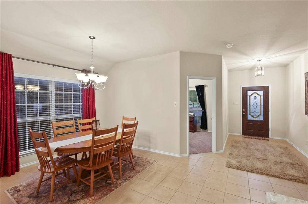 9609 Sand Trap Drive, McKinney, TX 75072 Entryway featuring a decorative glass front door and tile flooring, opening to a dining area with a multi-arm chandelier and a large window with blinds