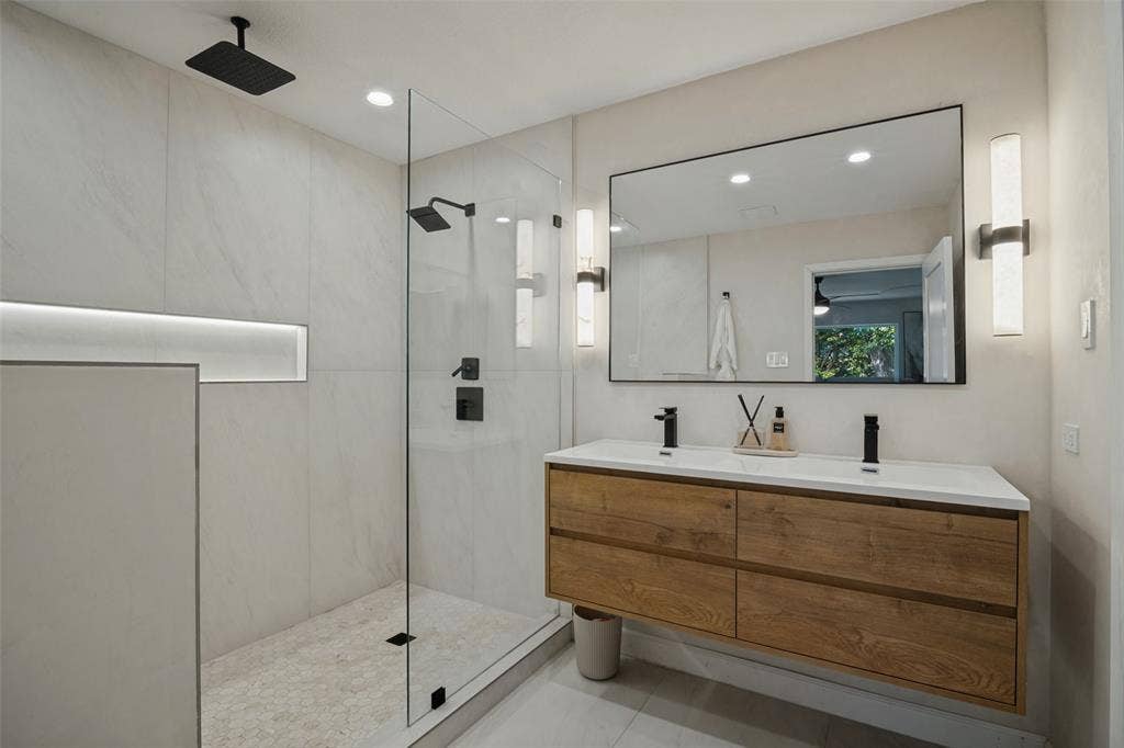 5021 Ashbrook Road, Dallas, TX 75227 Dual-sink floating vanity with wood-finish cabinetry, frameless mirror, and modern sconces
