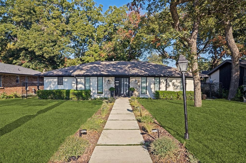 5021 Ashbrook Road, Dallas, TX 75227 White stone and stucco exterior with dark trim windows, a dark shingle roof, a dark entry door, and a concrete paver walkway