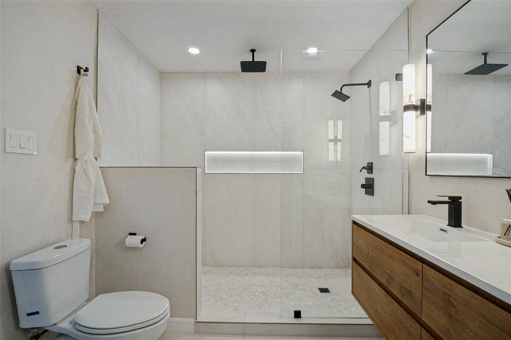 5021 Ashbrook Road, Dallas, TX 75227 Spa-inspired primary bathroom featuring a spacious walk-in shower with frameless glass enclosure, dual rainfall showerheads, and linear niche shelving