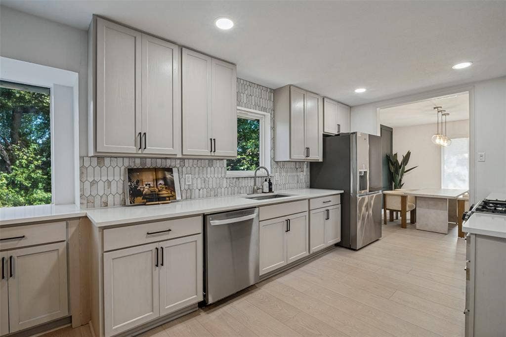 5021 Ashbrook Road, Dallas, TX 75227 Contemporary kitchen featuring light wood-finish flooring, white cabinetry with black hardware, white countertops, and a patterned tile backsplash