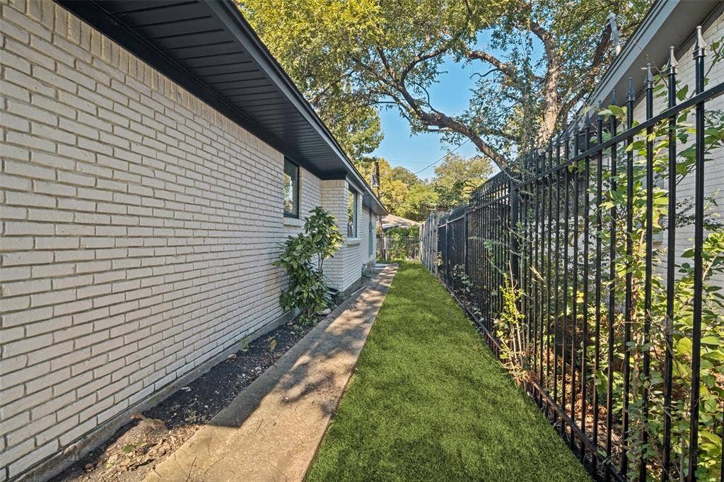 5021 Ashbrook Road, Dallas, TX 75227 White brick exterior, black soffit, black window trim, concrete pathway, and black metal fencing