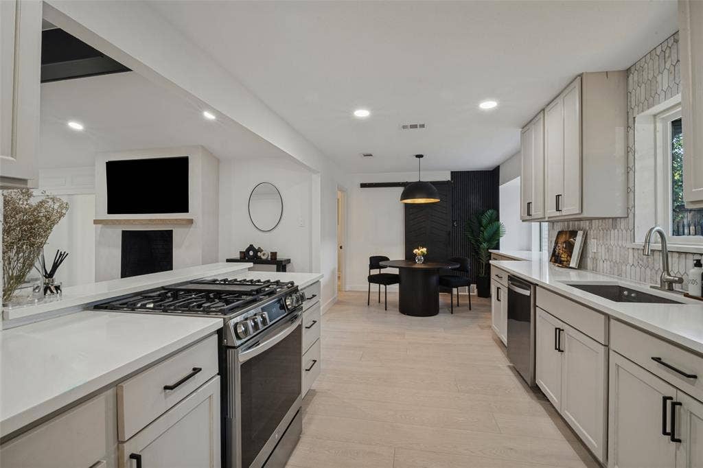 5021 Ashbrook Road, Dallas, TX 75227 Modern kitchen with light-toned wood-finish flooring, white cabinetry, integrated stainless-steel appliances, and a unique tiled backsplash