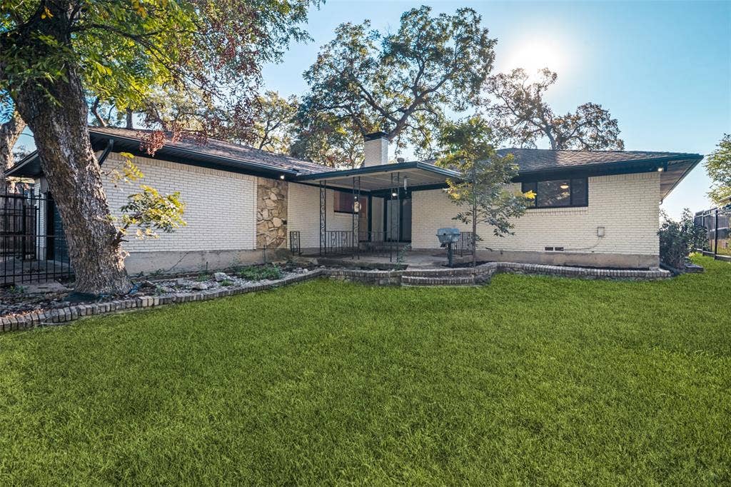 5021 Ashbrook Road, Dallas, TX 75227 Rear exterior with a covered patio, brick and stone facade, and a tiered retaining wall