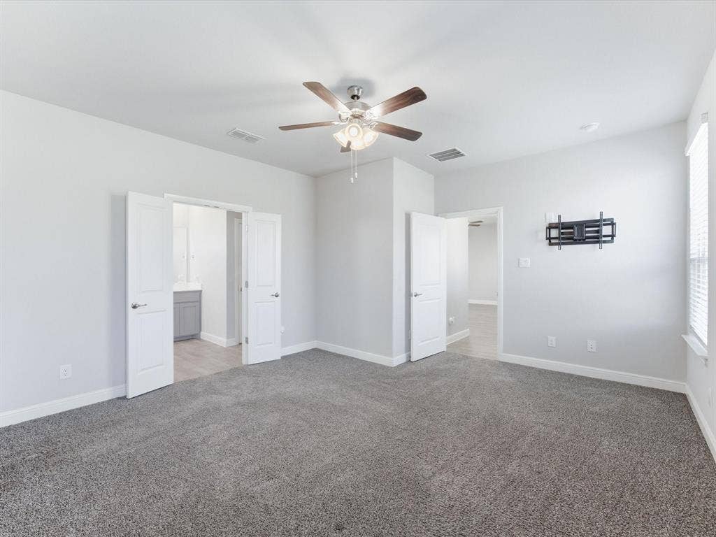 Spacious room featuring gray carpeting, a ceiling fan with integrated lighting, white walls, and white plantation shutters