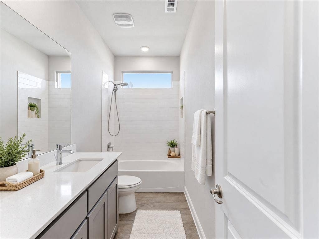 Vanity with a white countertop and undermount sink, wood-finish flooring, white subway tile shower surround, and built-in shower niche