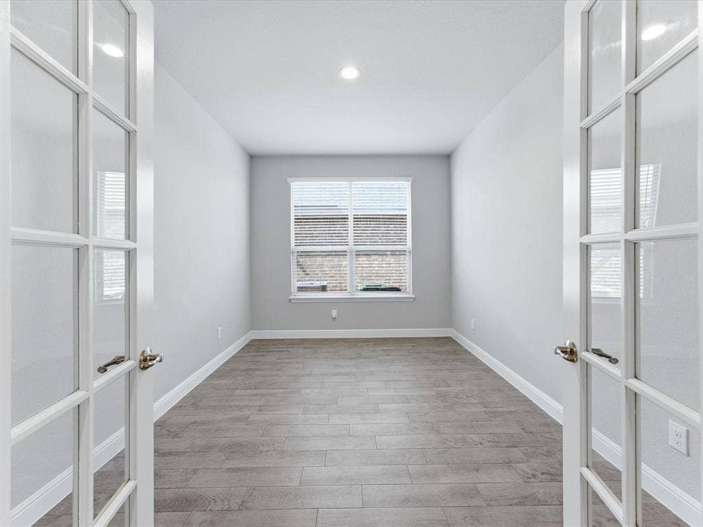Recessed lighting illuminates the room, featuring wood-finish flooring and a window with blinds