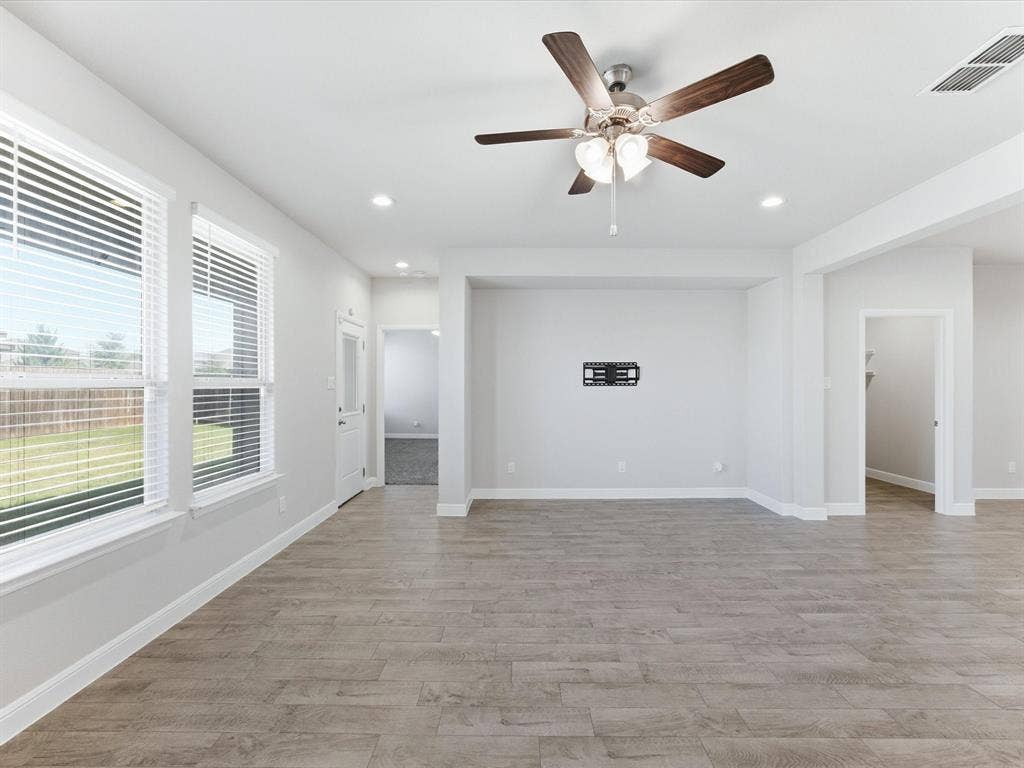 Spacious room featuring wood-finish flooring, multiple windows with blinds, a ceiling fan with integrated lighting, and recessed lighting