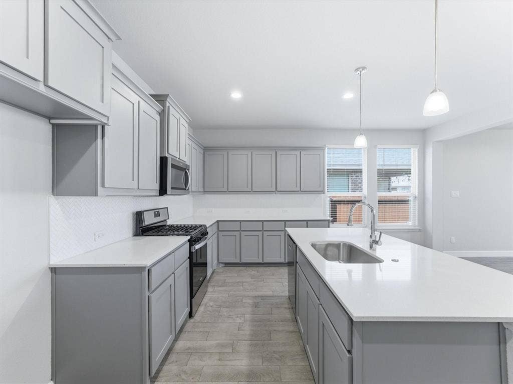Kitchen featuring gray shaker cabinetry, white countertops, a chevron pattern tile backsplash, a stainless steel sink, and stainless steel appliances