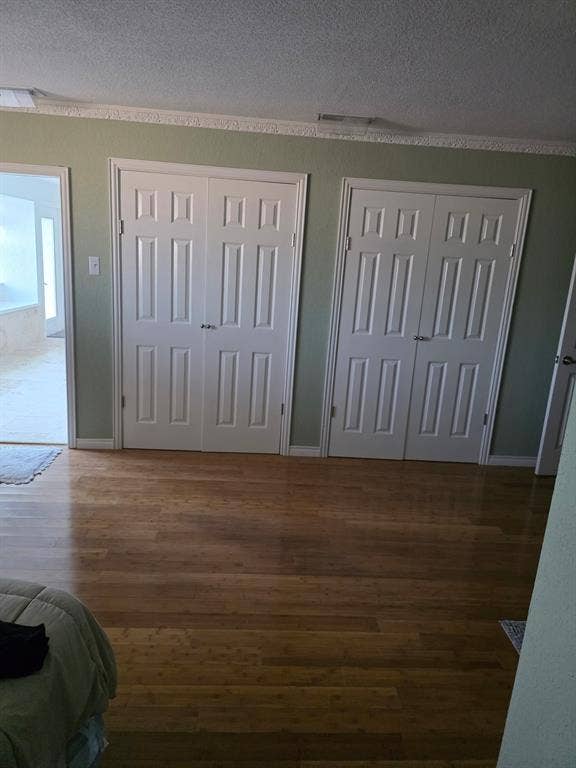 1608 University Drive, Richardson, TX 75081 Unfurnished bedroom featuring a textured ceiling, baseboards, multiple closets, and wood finished floors