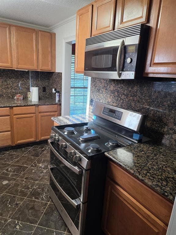 1608 University Drive, Richardson, TX 75081 Kitchen featuring dark stone counters, appliances with stainless steel finishes, marble finish floor, and tasteful backsplash