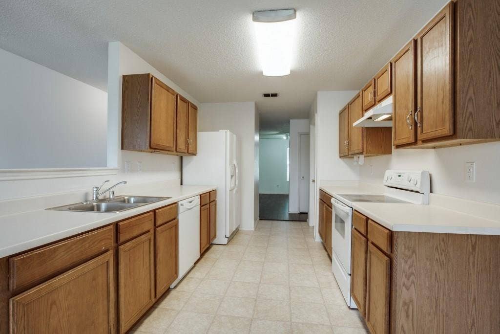 2800 Bissell Way, Wylie, TX 75098 Galley kitchen featuring wood-finish cabinetry, white countertops, and white appliances