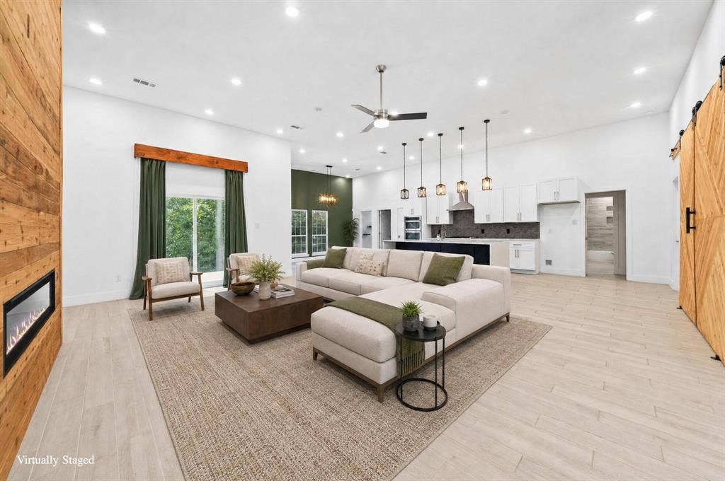 Expansive open-concept living area featuring a linear fireplace with a wood-paneled surround, light-toned wood-finish flooring, and recessed lighting