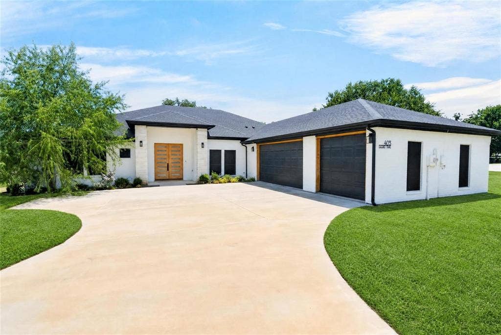 Modern exterior with white brick finish, dark shingle roof, wood-tone double entry doors, and a concrete driveway