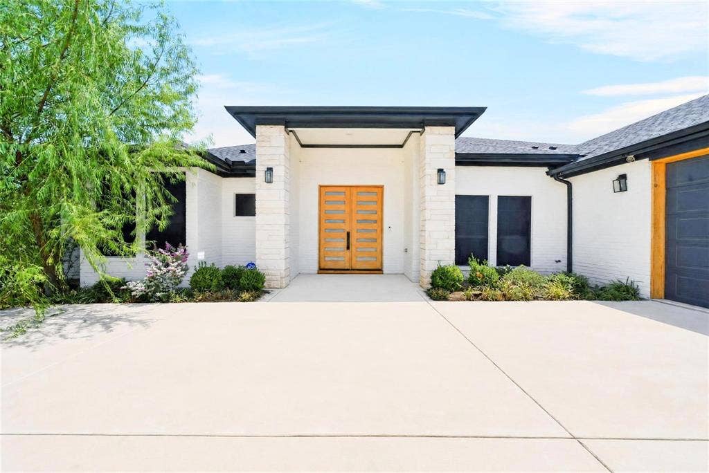 White brick exterior with stone accents, a modern double wooden entry door, and a dark-toned garage door