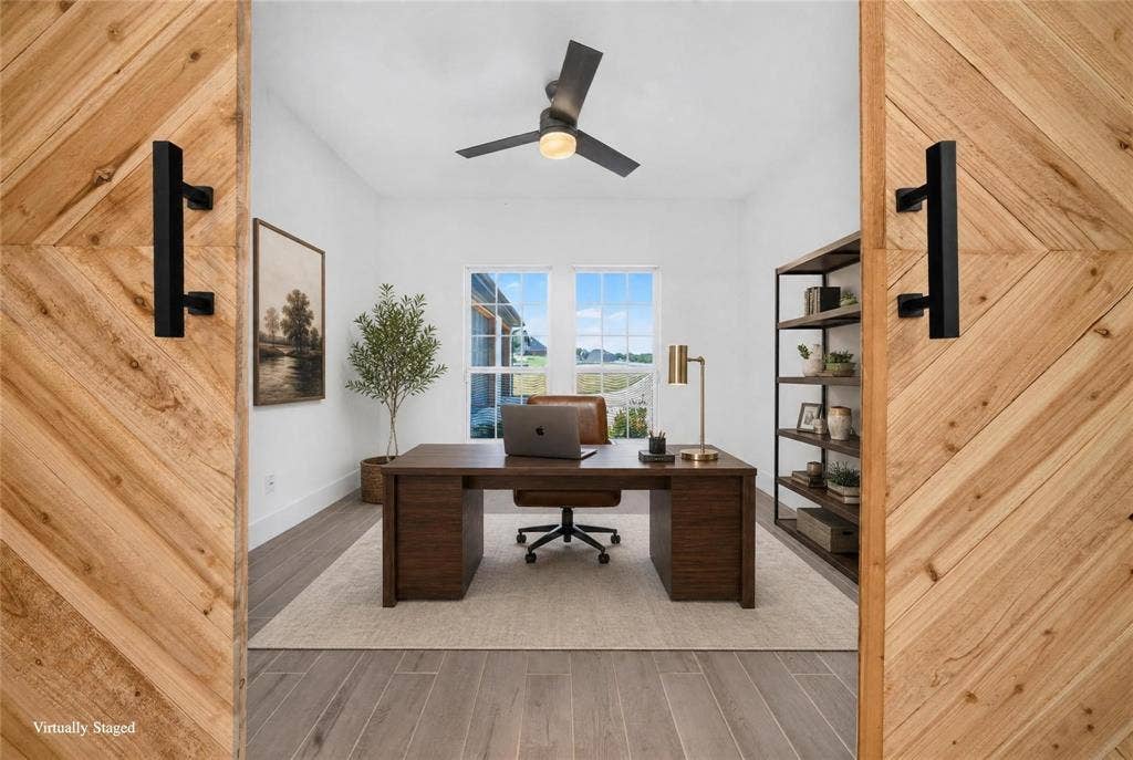 Chevron wood-finish barn doors with matte black hardware, wood-finish flooring, a contemporary ceiling fan, and large windows