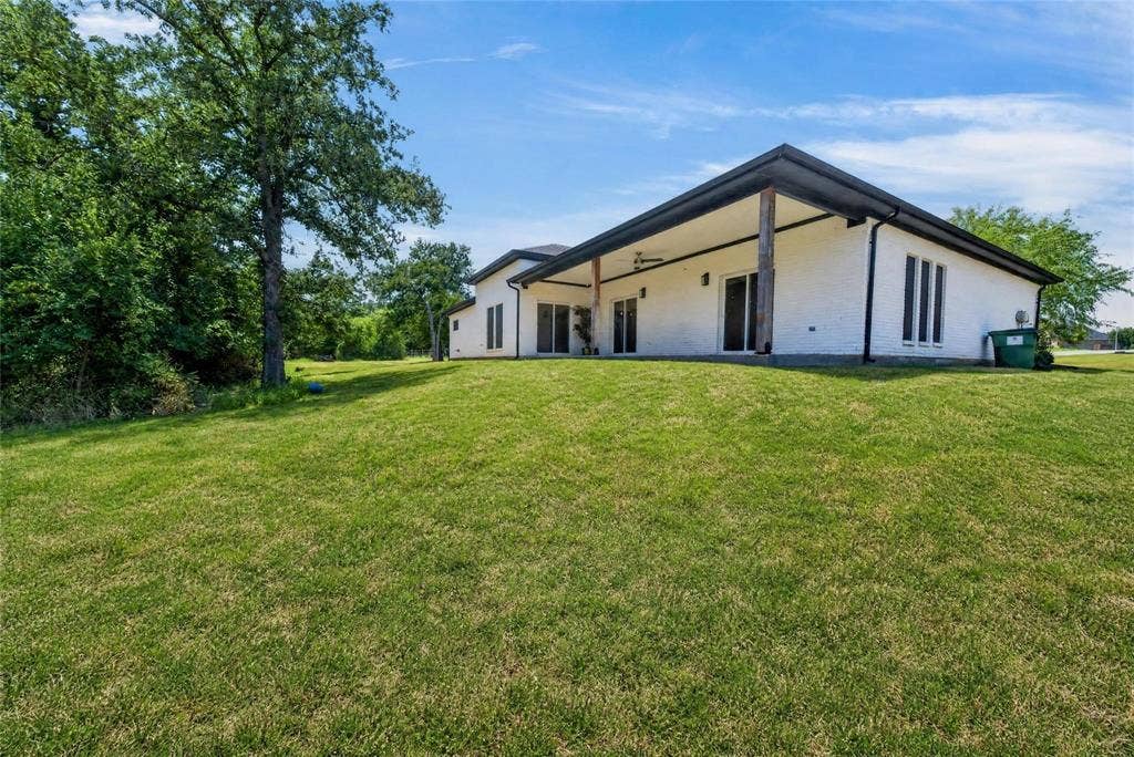 Expansive lawn area, white brick exterior, black trim roofline, covered patio, wood support columns