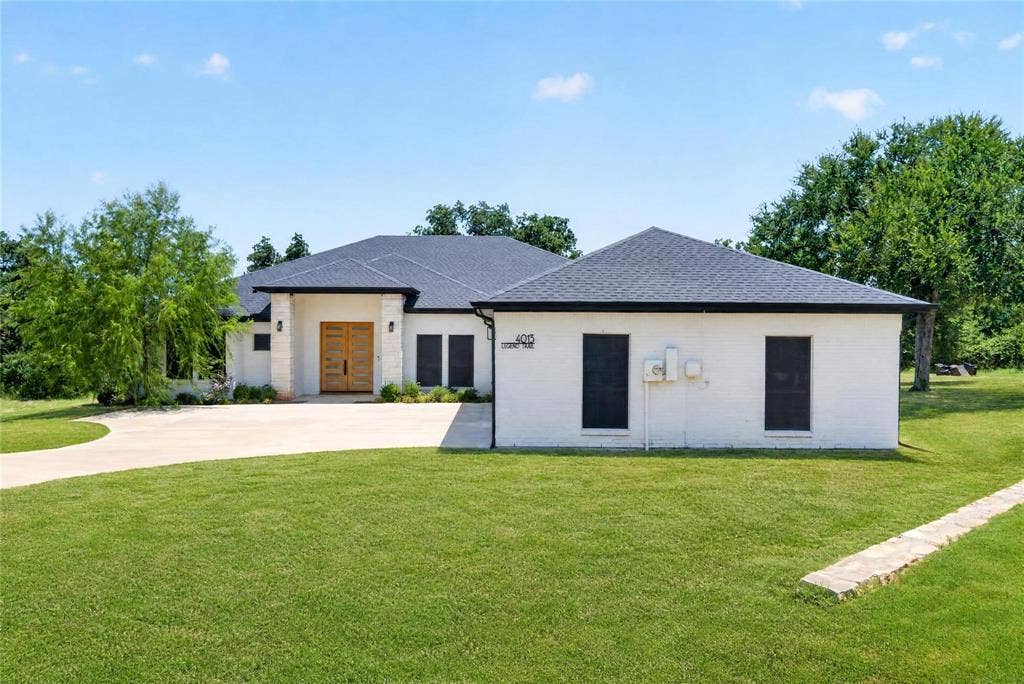 White brick exterior with a dark-pitched roof, a light wood-finish double-door entry, and a curved paved driveway