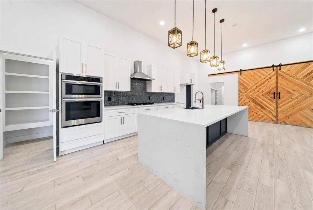 Modern kitchen with a waterfall island, light wood-finish flooring, white cabinetry, stainless steel appliances, and a dark stone backsplash