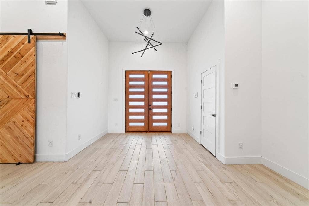 Vaulted ceiling with a contemporary chandelier, light wood-finish flooring, and a natural wood barn door