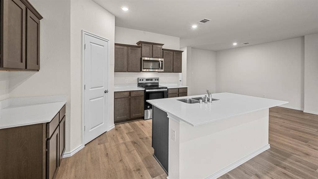 810 Parksville Drive, Ferris, TX 75125 Kitchen featuring dark wood-finish cabinetry, light countertops, a kitchen island with an undermount dual-basin sink, stainless steel appliances, and recessed lighting