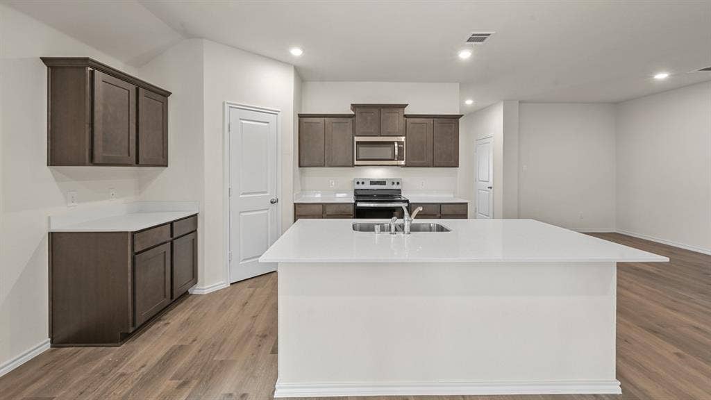 810 Parksville Drive, Ferris, TX 75125 Open-concept kitchen featuring an island with a stainless steel sink, wood-finish flooring, dark wood cabinetry, and stainless steel appliances