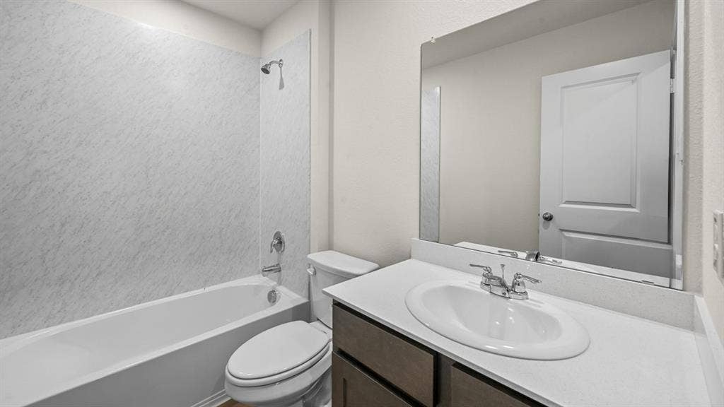 810 Parksville Drive, Ferris, TX 75125 Bathroom featuring a white tub and shower combination with textured wall surround, a toilet, a vanity with a drop-in sink, and a large wall-mounted mirror