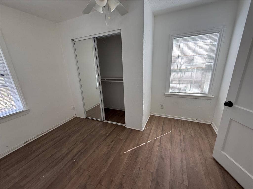 2952 Bardwell Avenue, Dallas, TX 75216 Wood-finish flooring throughout, white walls, two windows with blinds, mirrored sliding closet doors, and a ceiling fan