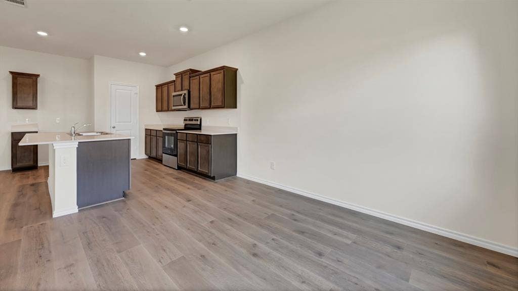 231 Yates Street, Bullard, TX 75757 Modern kitchen featuring wood-finish flooring, dark wood cabinetry, and a central island with a sink and light-toned countertop
