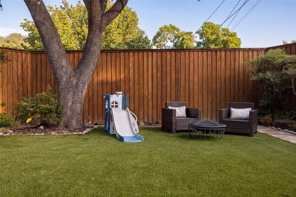 10945 Middle Knoll Drive, Dallas, TX 75238 Private backyard featuring a full perimeter wood fence, mature tree, and artificial turf