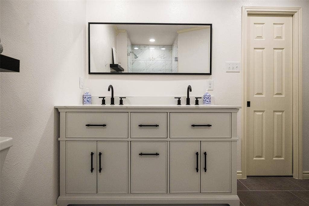 10945 Middle Knoll Drive, Dallas, TX 75238 Dual vanity with white countertop, matte black fixtures, and cabinet storage