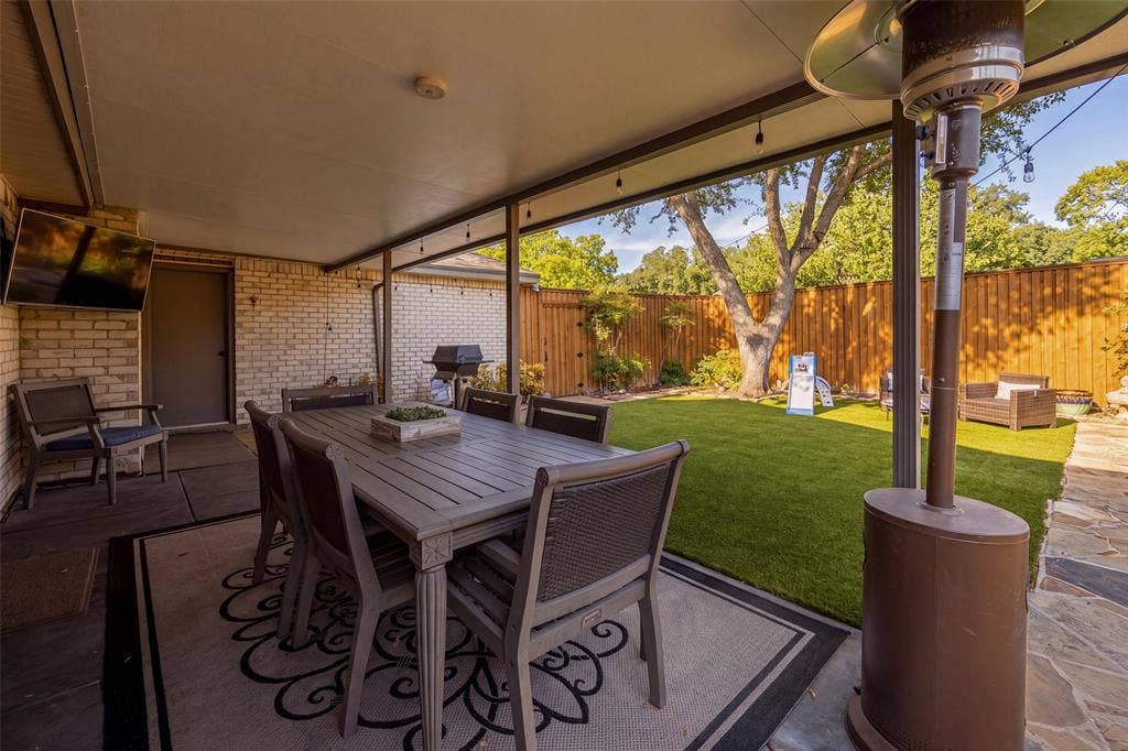 10945 Middle Knoll Drive, Dallas, TX 75238 Covered patio featuring string lighting, brick exterior wall, and an expansive lawn with mature trees and wood fencing