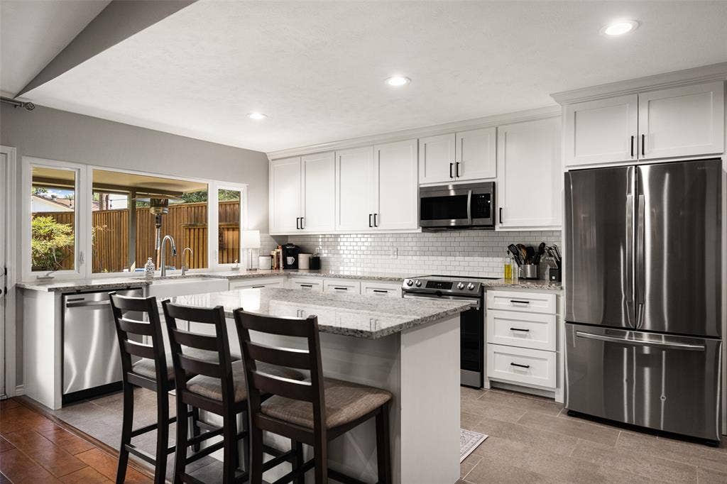 10945 Middle Knoll Drive, Dallas, TX 75238 Modern kitchen featuring white shaker cabinetry, stainless steel appliances, a center island with countertop seating, and a subway tile backsplash