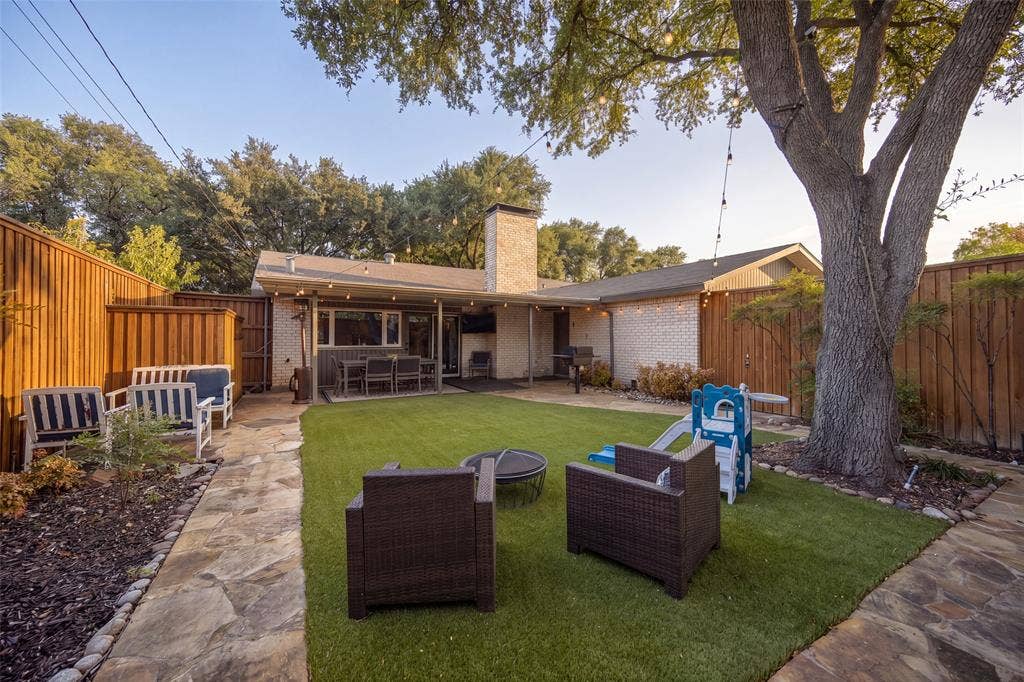 10945 Middle Knoll Drive, Dallas, TX 75238 Manicured backyard featuring a stone patio, artificial turf, a mature tree, and privacy fencing