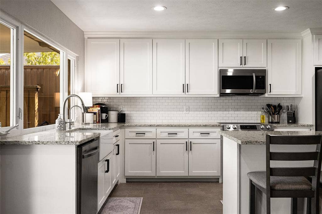 10945 Middle Knoll Drive, Dallas, TX 75238 White shaker cabinetry, granite countertops, stainless steel appliances, subway tile backsplash, and recessed lighting