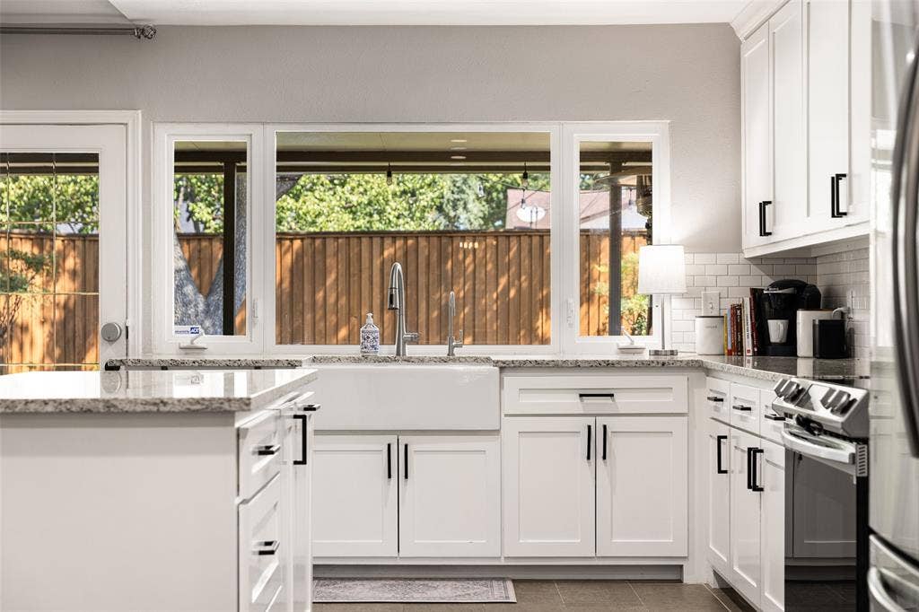 10945 Middle Knoll Drive, Dallas, TX 75238 White shaker-style cabinetry with matte black hardware, stone-finish countertops, stainless steel appliances, and a farmhouse sink