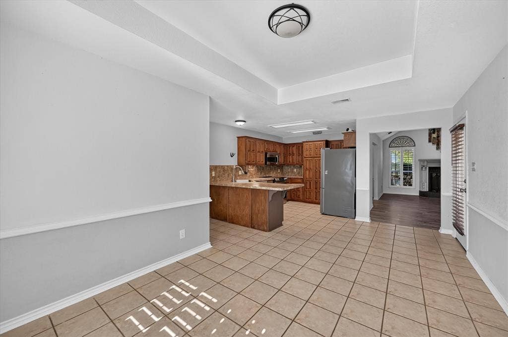 Tiled flooring throughout, kitchen featuring wood cabinetry and an integrated microwave, and an arched doorway leading to an additional space with a large arched window