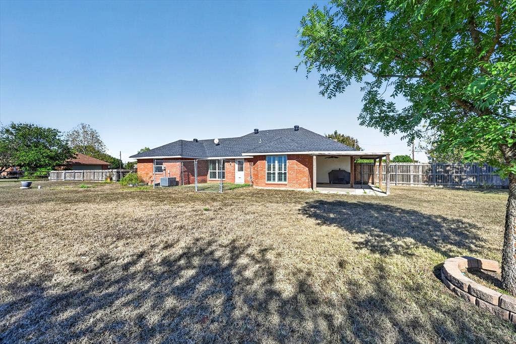Expansive backyard featuring a red brick exterior, covered patio, and mature trees