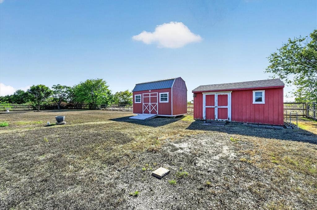 Two red storage sheds with white trim, one featuring a gambrel roof and the other a gabled roof