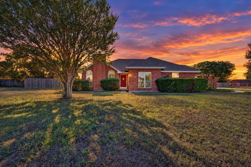 Brick exterior with a red front door, large front yard, and mature landscaping