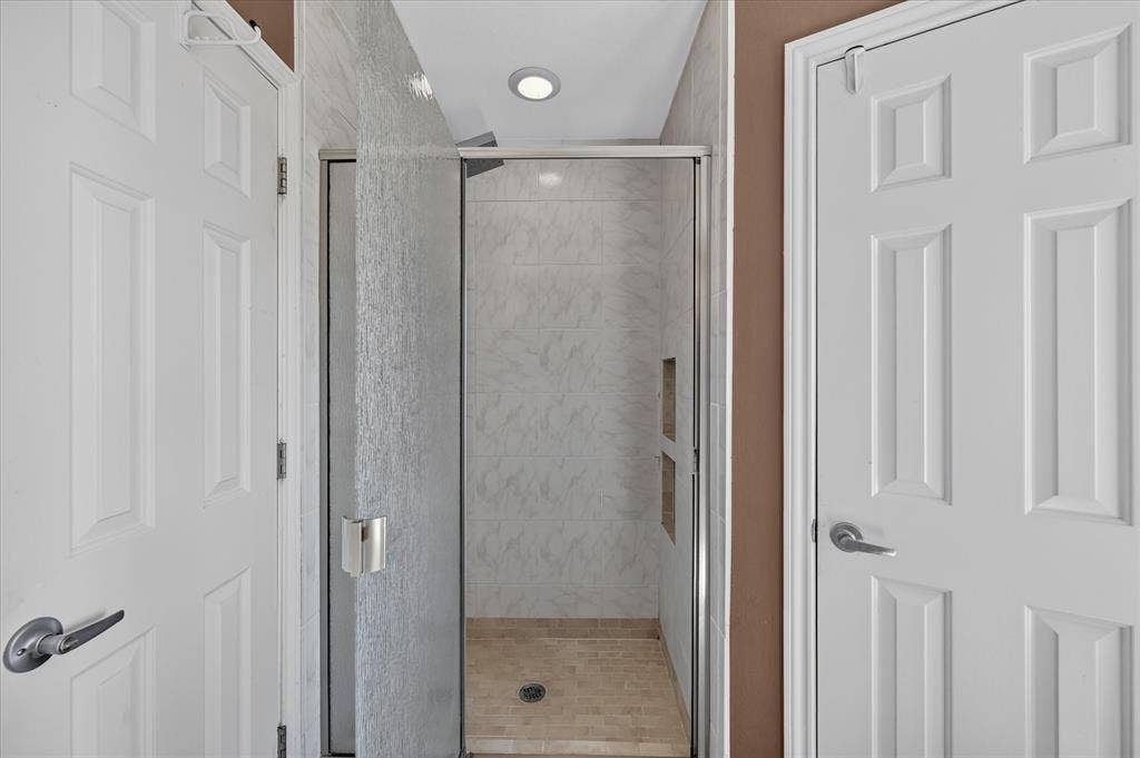 Enclosed shower with clear glass door, built-in shelving, tiled walls, and recessed lighting