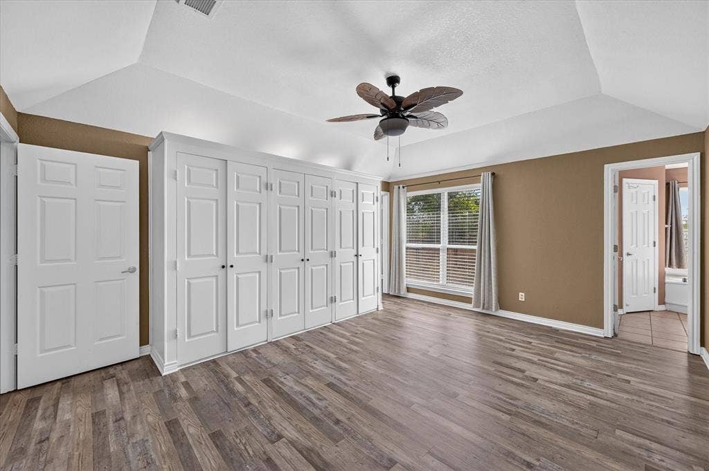 Vaulted ceilings, wood-finish flooring, built-in storage cabinetry, ceiling fan, and a window with blinds