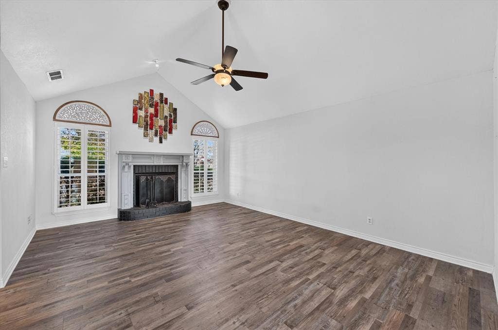 Vaulted ceiling, wood-finish flooring, fireplace with a tile hearth, window shutters, and a ceiling fan with integrated lighting