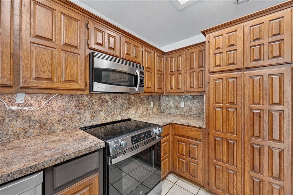 Extensive wood-finish cabinetry, stainless steel microwave, and cooktop with integrated oven