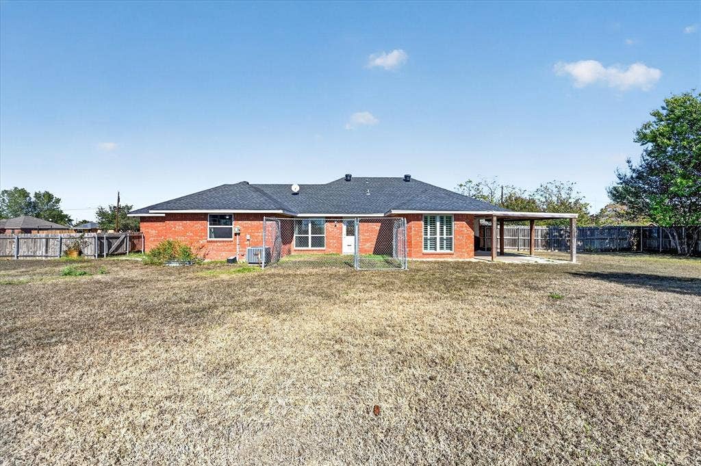 Red brick exterior, dark shingle roof, covered patio structure, fenced yard perimeter