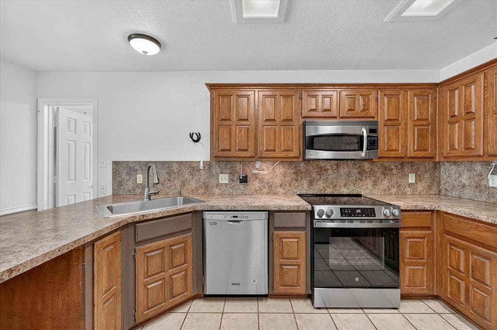 Kitchen featuring wood cabinetry, stainless steel appliances, a corner sink, and tiled flooring