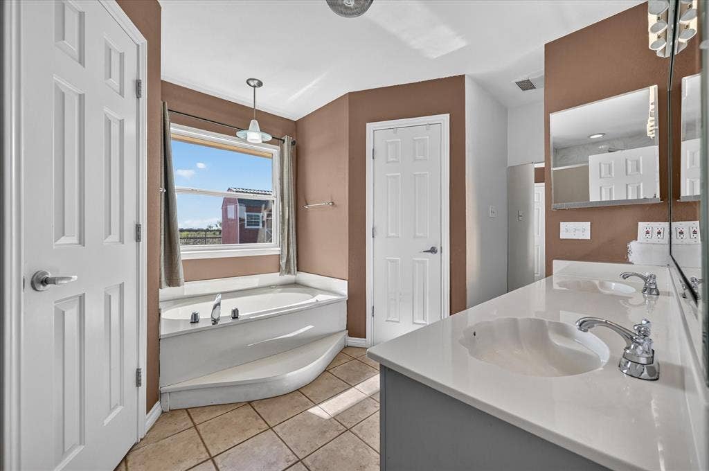 Dual vanity with integrated sinks, polished chrome fixtures, built-in soaking tub, his and her walk in closets, and tile flooring