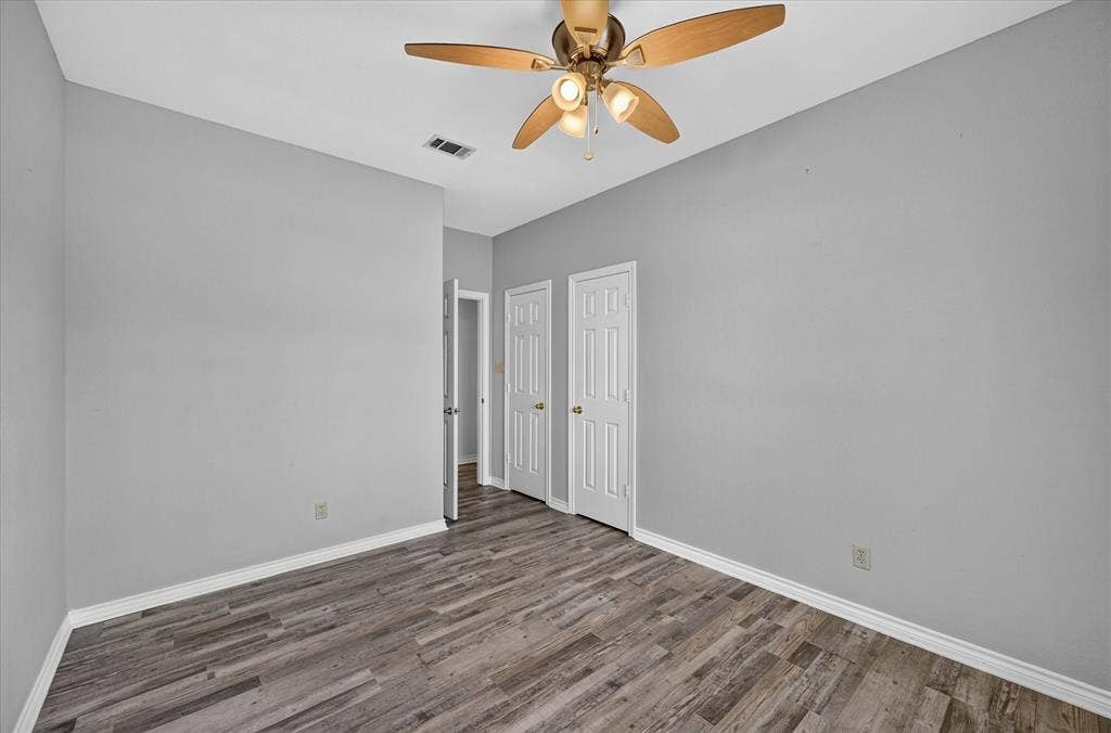 Wood-finish flooring, light gray walls, white trim, ceiling fan with integrated lighting, and white paneled doors