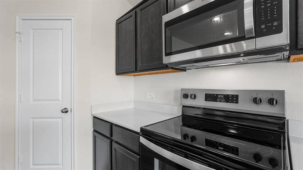 189 Brooks Street, Bullard, TX 75757 Stainless steel microwave, electric range, dark wood-finish cabinetry, and solid surface countertops