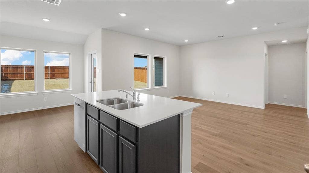 189 Brooks Street, Bullard, TX 75757 Kitchen island with dual stainless steel sink, light-toned countertops, wood-finish flooring, recessed lighting, and multiple windows